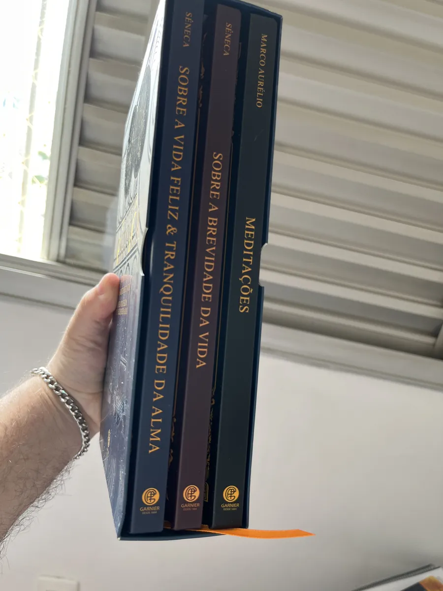 Três livros do box Biblioteca Estoica vistos de lado na mão de um cliente